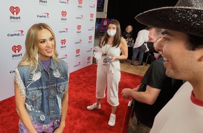 Carrie Underwood on the iHeartCountry Festival carpet, with Ricky in frame at the right.