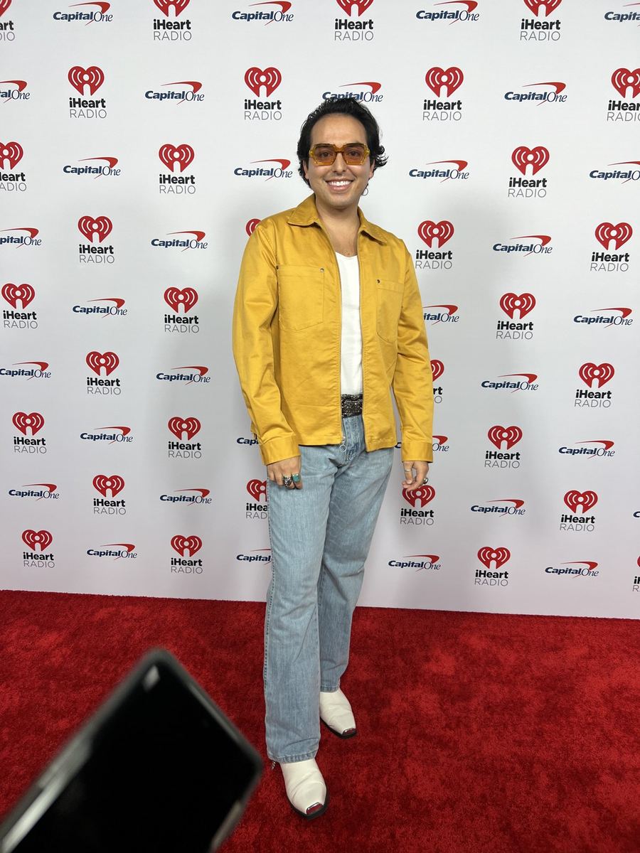Ricky Garcia on the iHeartRadio step-and-repeat in a yellow jacket and tinted glasses.