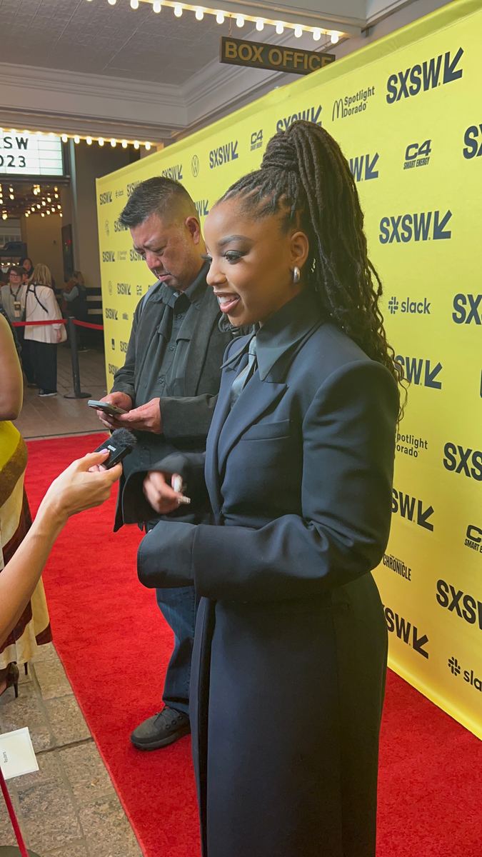 Halle Bailey in a navy coat on the SXSW 2023 carpet, speaking to someone holding a microphone.