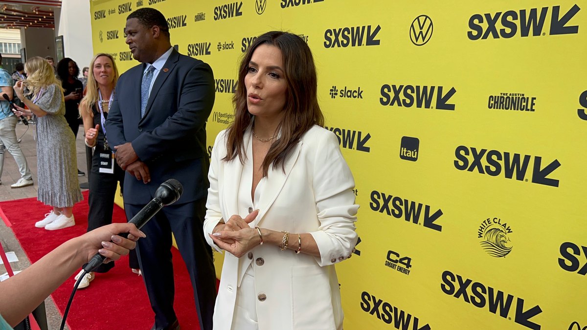 Eva Longoria mid-answer on the SXSW carpet, speaking into a microphone held from off-frame.